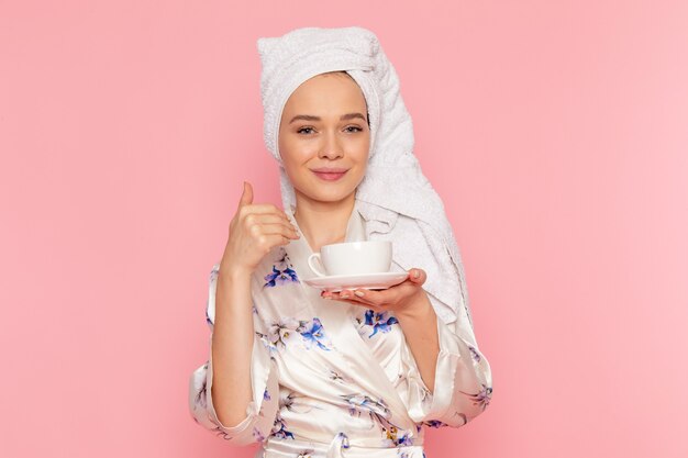 Una vista frontal hermosa jovencita en bata de baño con taza de café