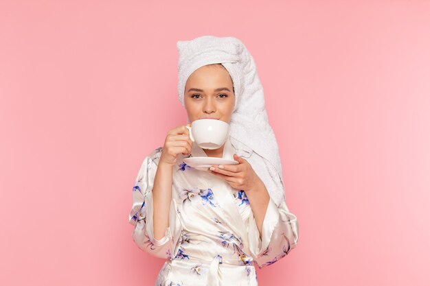 Una vista frontal hermosa jovencita en bata de baño tomando café con una sonrisa en su rostro