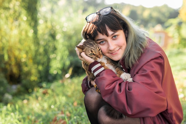 Vista frontal de la hermosa mujer abrazando a su gato atigrado en el parque