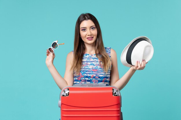 Vista frontal hermosa mujer preparándose para las vacaciones con gafas de sol y sombrero en el espacio azul