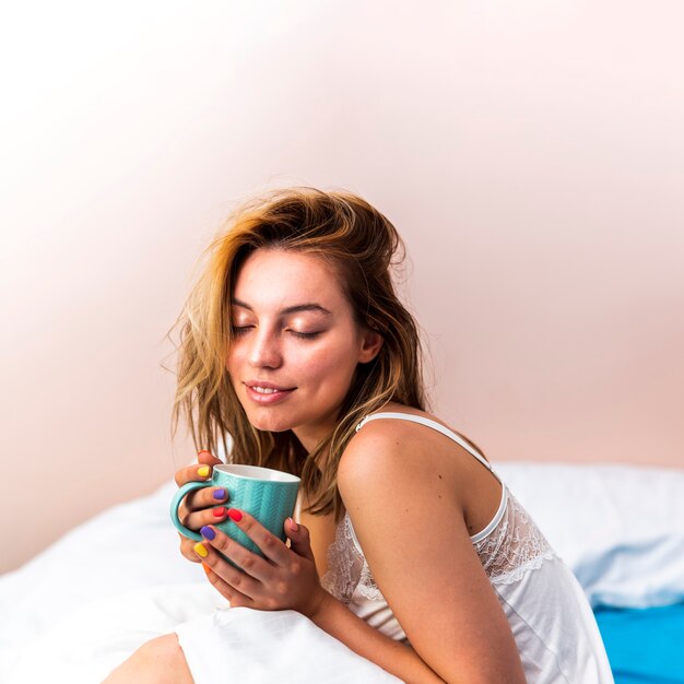 Vista frontal hermosa mujer sosteniendo una taza en la cama