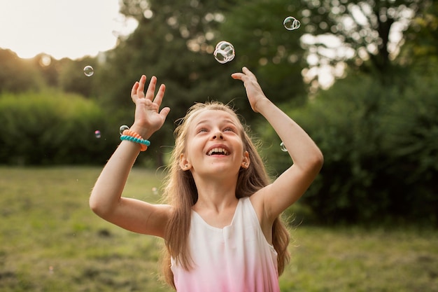 Vista frontal de la hermosa niña feliz con pompas de jabón