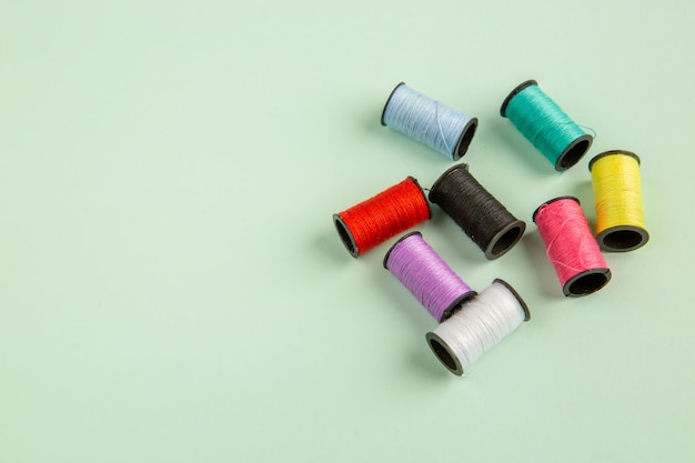 Vista frontal hilos de colores sobre la superficie verde coser ropa color coser aguja pin