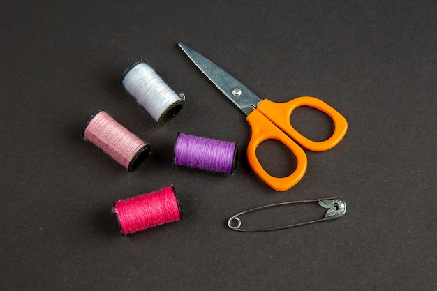Vista frontal hilos de colores con tijeras en la superficie oscura oscuridad ropa coser tejer color mujer coser pin foto