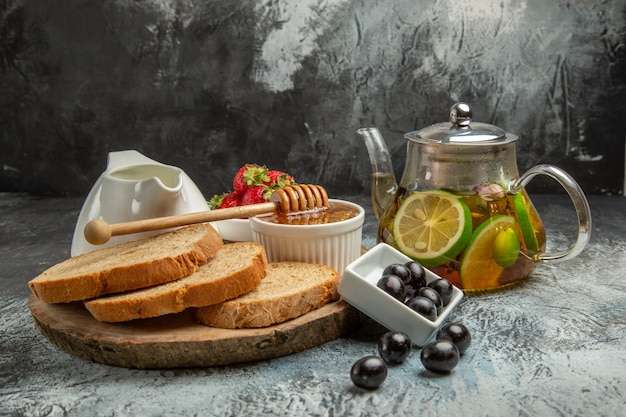 Vista frontal de hogazas de pan con miel, aceitunas y té en superficie ligera, comida para el desayuno dulce