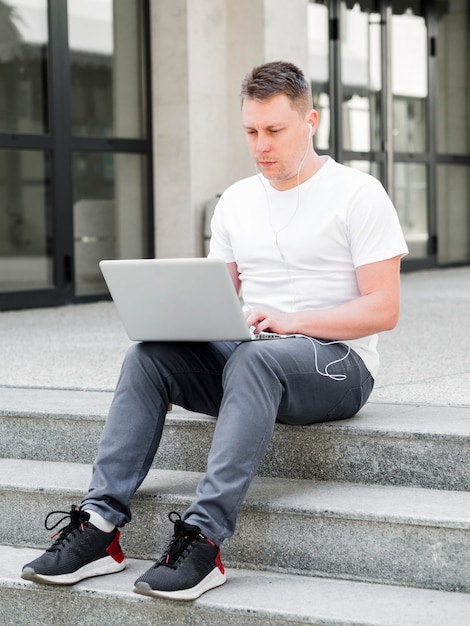 Vista frontal del hombre al aire libre en pasos trabajando en la computadora portátil