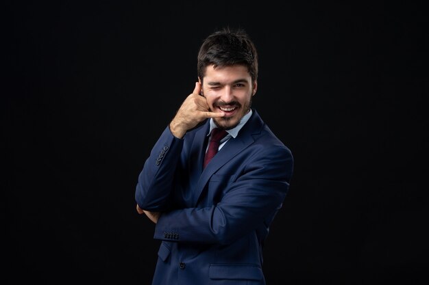 Vista frontal del hombre barbudo emocional haciendo gesto de anteojos en la pared oscura aislada