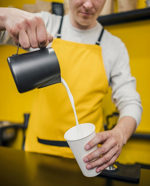 Vista frontal del hombre barista vertiendo leche en la taza