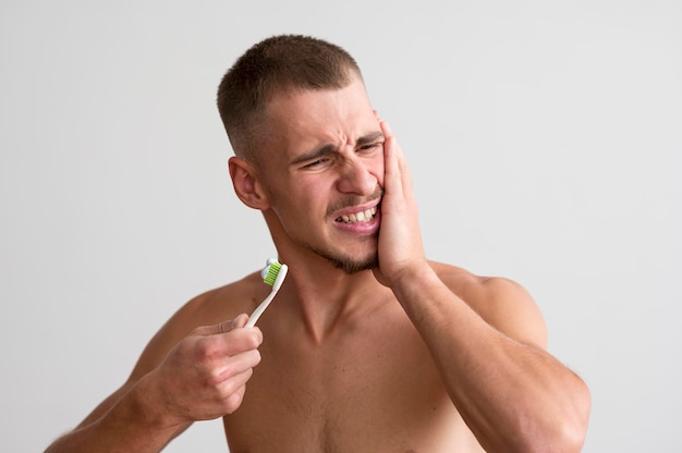 Vista frontal del hombre sin camisa con dolor de muelas y sosteniendo el cepillo de dientes