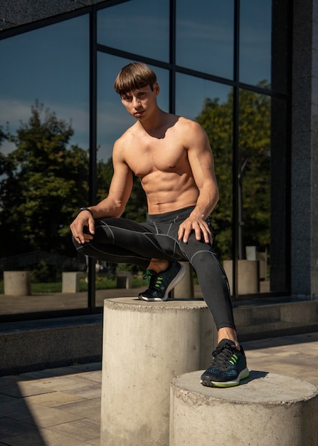 Vista frontal del hombre sin camisa posando al aire libre mientras hace ejercicio