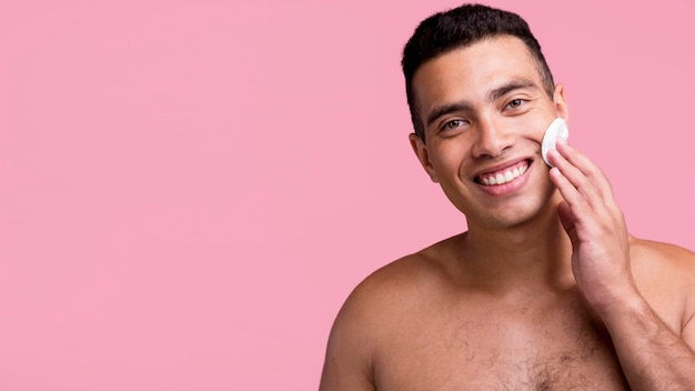 Vista frontal del hombre sin camisa sonriente con almohadillas de algodón en su rostro