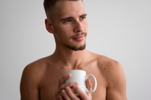 Vista frontal del hombre sin camisa con taza de café en la mañana
