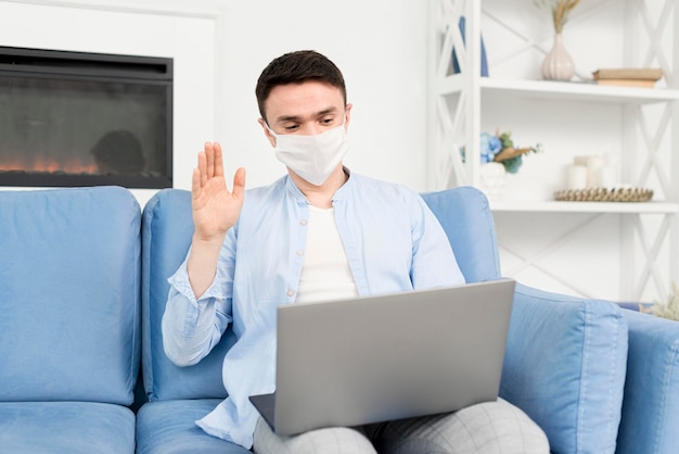 Vista frontal del hombre en casa con máscara médica trabajando en la computadora portátil