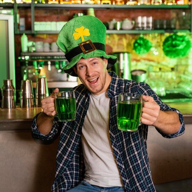 Vista frontal del hombre celebrando st. patrick's day en el bar con bebidas