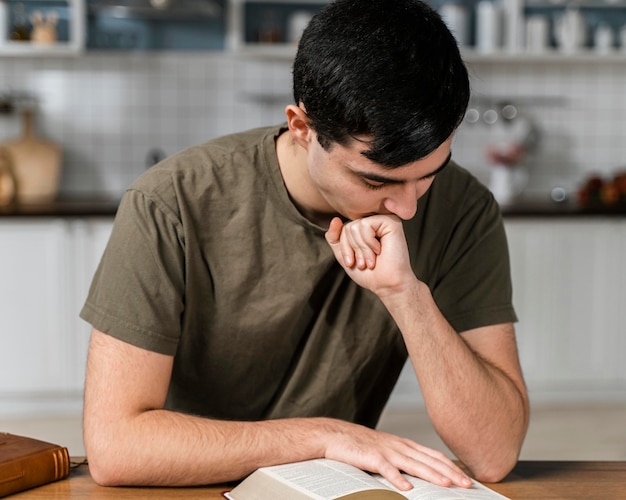Vista frontal del hombre en la cocina leyendo la Biblia