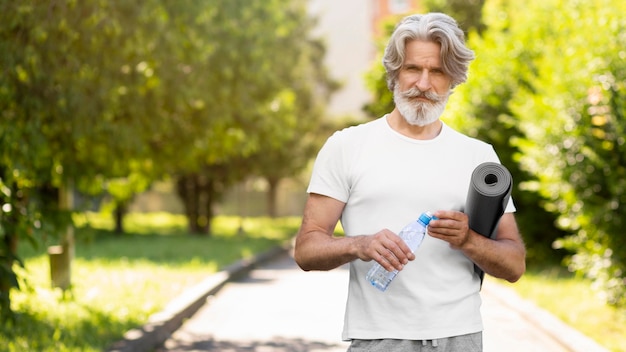 Vista frontal hombre con colchoneta de yoga y agua