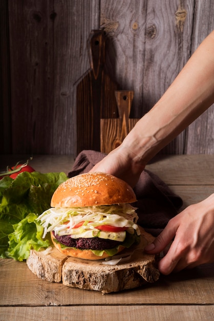 Vista frontal hombre colocando una hamburguesa en una tabla de madera