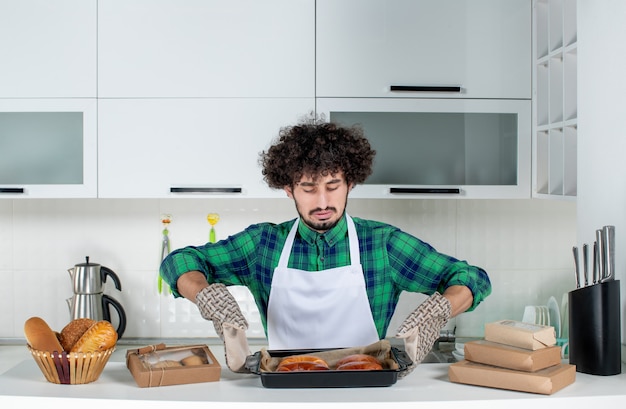 Foto gratuita vista frontal del hombre concentrado con soporte sosteniendo pasteles recién horneados en la cocina blanca