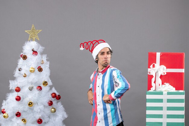 Vista frontal del hombre confiado poniendo las manos en la cintura cerca del árbol de Navidad blanco