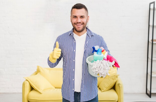 Foto gratuita vista frontal del hombre dando pulgares mientras sostiene productos de limpieza