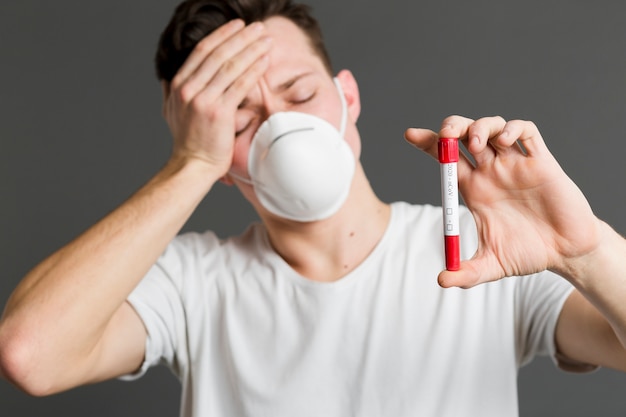 Vista frontal del hombre enfermo con una máscara médica y sosteniendo vacutainer