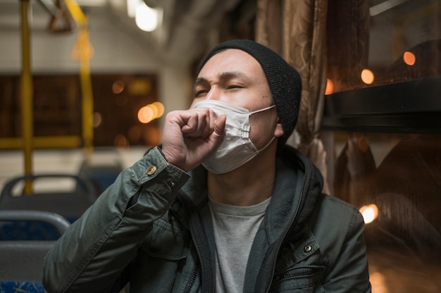Vista frontal del hombre enfermo tosiendo en el autobús mientras usa una máscara médica