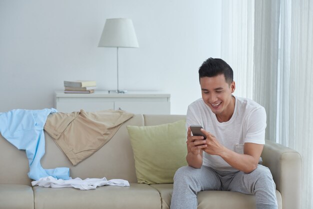 Vista frontal del hombre enviando mensajes de texto a amigos en casa y sonriendo