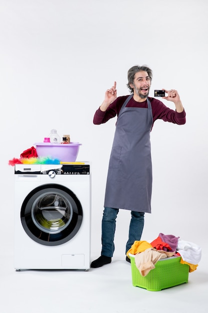 Foto gratuita vista frontal del hombre feliz que sostiene la tarjeta de pie cerca de la lavadora sobre fondo blanco.