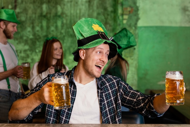 Vista frontal del hombre feliz con sombrero celebrando st. día de patricio con bebida en el bar.