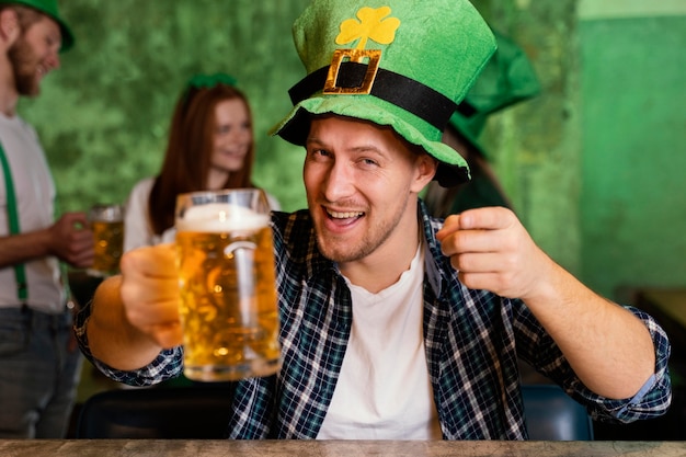 Vista frontal del hombre feliz con sombrero celebrando st. día de patrick en el bar