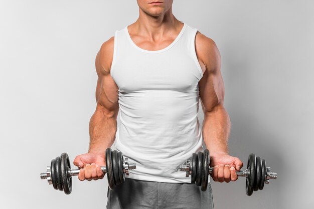 Vista frontal del hombre en forma con camiseta sin mangas trabajando con pesas