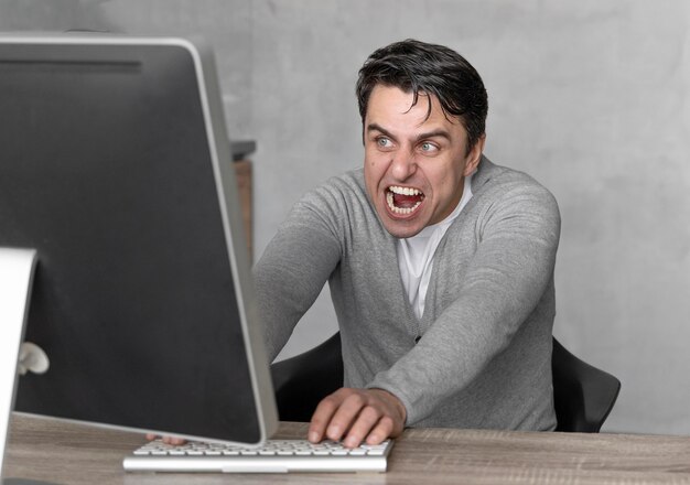 Vista frontal del hombre frustrado que trabaja en el campo de los medios con la computadora