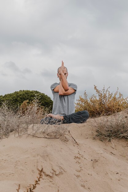 Vista frontal del hombre fuera meditando mientras hace yoga