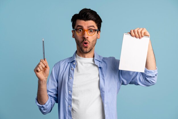 Vista frontal del hombre con gafas que tiene una idea mientras sostiene el cuaderno y la pluma