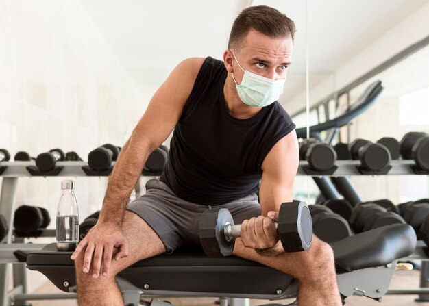 Vista frontal del hombre en el gimnasio con máscara médica trabajando