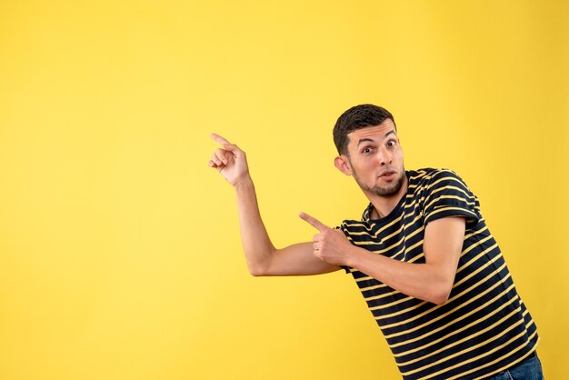 Vista frontal hombre guapo en camiseta a rayas blanco y negro apuntando a algo sobre fondo amarillo aislado