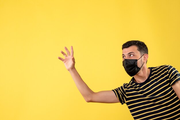 Vista frontal hombre guapo en máscara negra saludando a alguien sobre fondo amarillo aislado