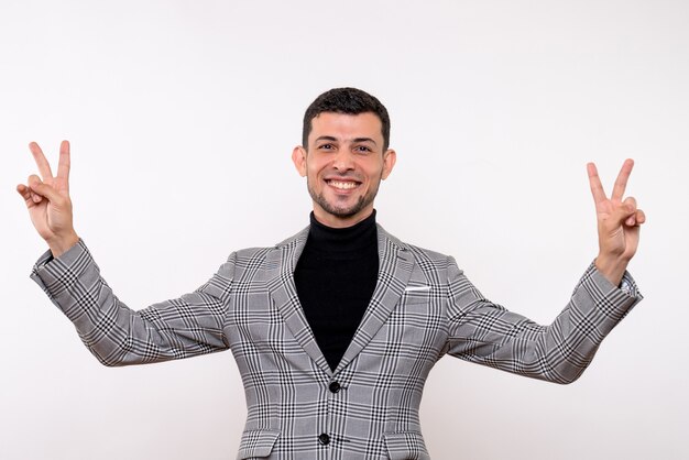 Vista frontal del hombre guapo en traje haciendo el signo de la victoria de pie sobre fondo blanco.