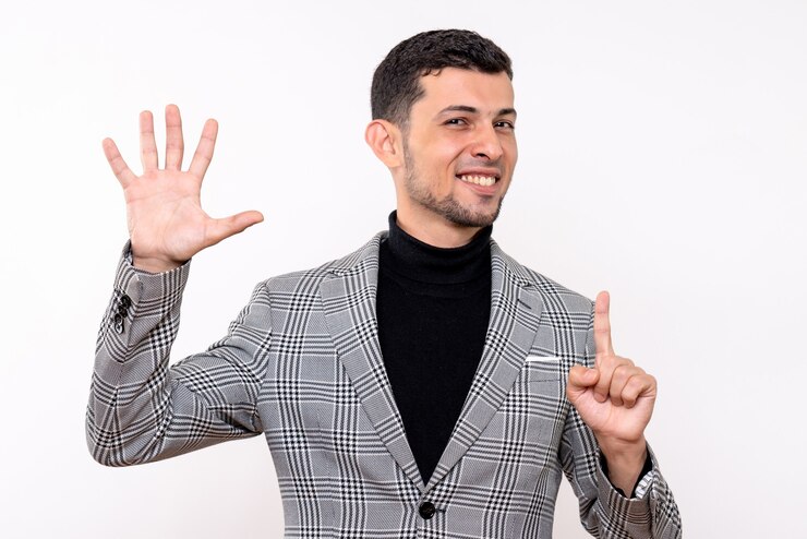 Vista frontal hombre guapo en traje levantando la mano de pie sobre fondo blanco aislado
