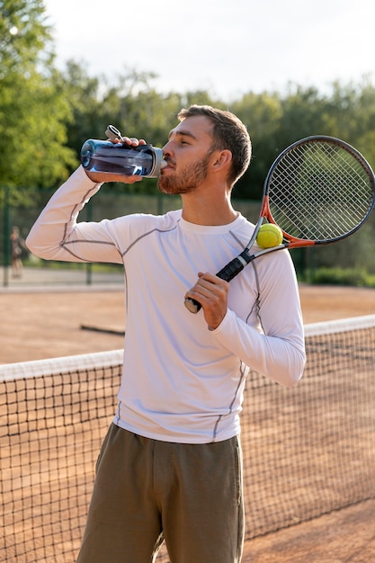 Vista frontal hombre hidratante en cancha de tenis