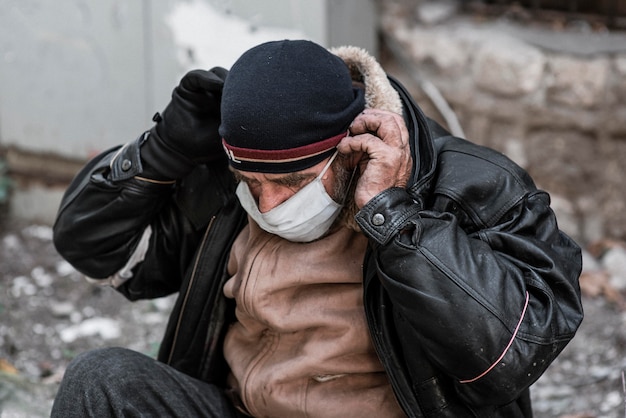 Vista frontal del hombre sin hogar al aire libre poniéndose máscara médica