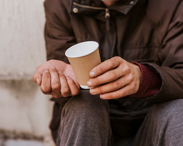 Vista frontal del hombre sin hogar sosteniendo la taza