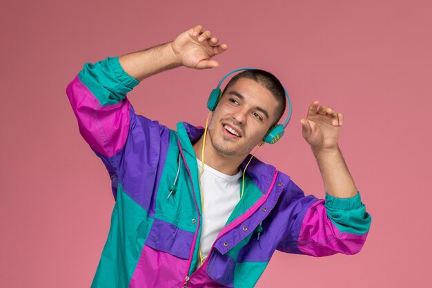 Vista frontal del hombre joven en abrigo colorido escuchando música con movimientos de baile en el fondo rosa