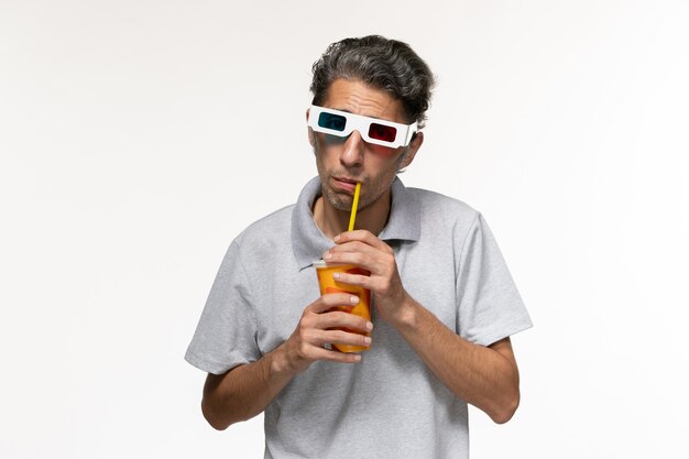 Vista frontal del hombre joven bebiendo refrescos y viendo la película en d gafas de sol en el escritorio blanco