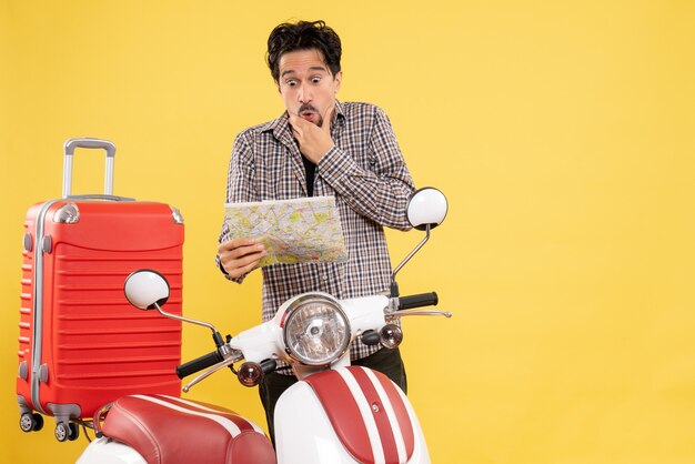 Vista frontal del hombre joven con bicicleta observando el mapa con expresión de sorpresa en amarillo