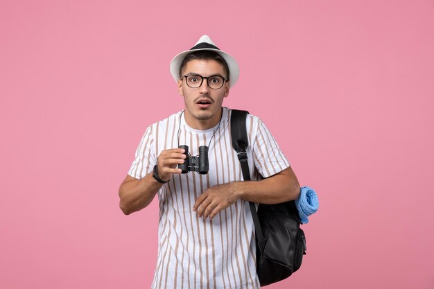 Vista frontal del hombre joven con bolsa y binoculares sobre fondo rosa claro