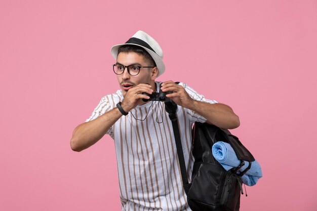 Vista frontal del hombre joven con bolsa y binoculares sobre fondo rosa claro