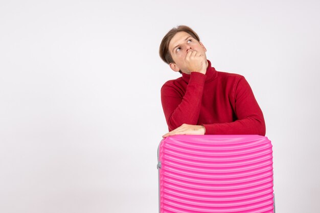 Vista frontal del hombre joven con bolsa rosa pensando sobre fondo blanco.