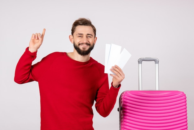 Vista frontal del hombre joven con bolsa rosa y sosteniendo boletos en la pared blanca viaje de vacaciones viaje de vuelo turista de verano