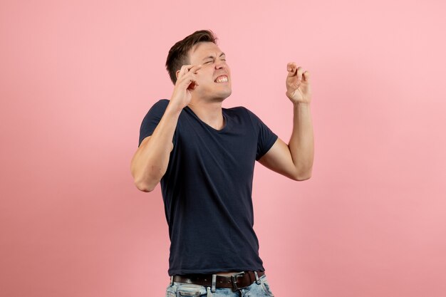 Vista frontal hombre joven en camisa azul oscuro cruzando los dedos sobre fondo rosa emoción masculina modelo humano color hombre